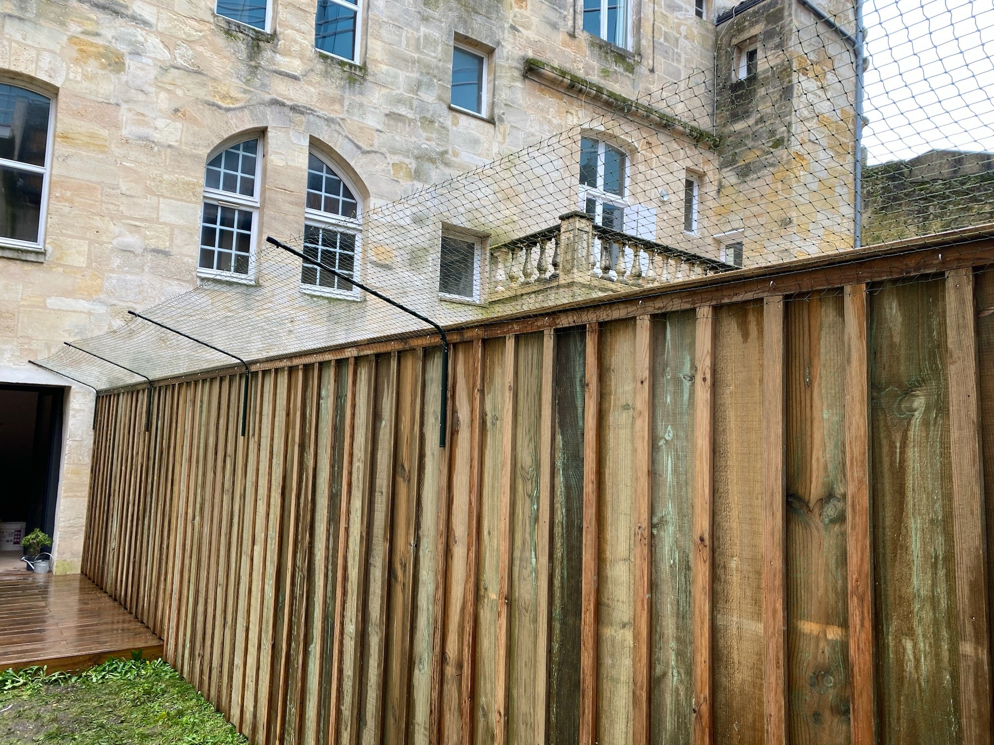 Palissade en bois surmontée de bavolet anti-fugue devant bâtiment en pierre